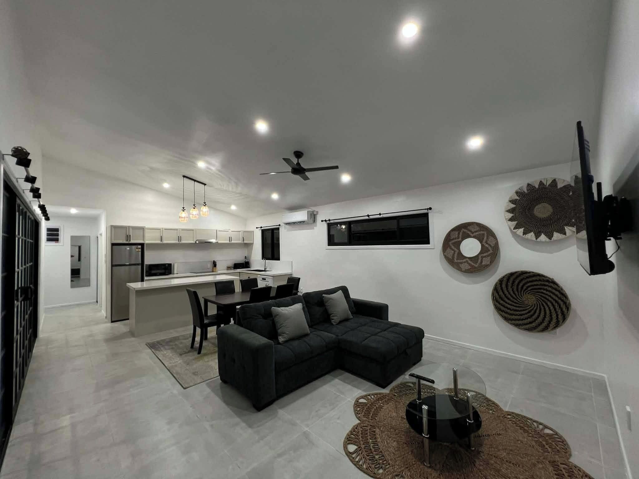 Una cocina moderna con comedor, un sofá seccional negro y decoración en la pared.