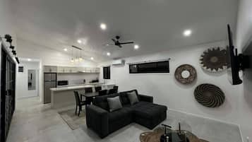 Una cocina moderna con comedor, un sofá seccional negro y decoración en la pared.