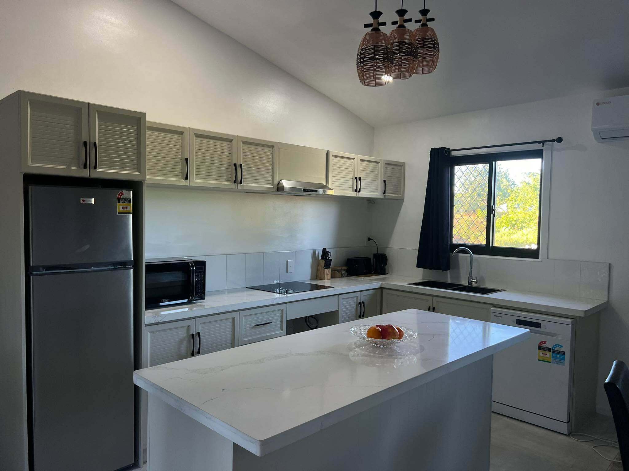 A modern kitchen with a central island, stainless steel appliances, and a window with curtains.