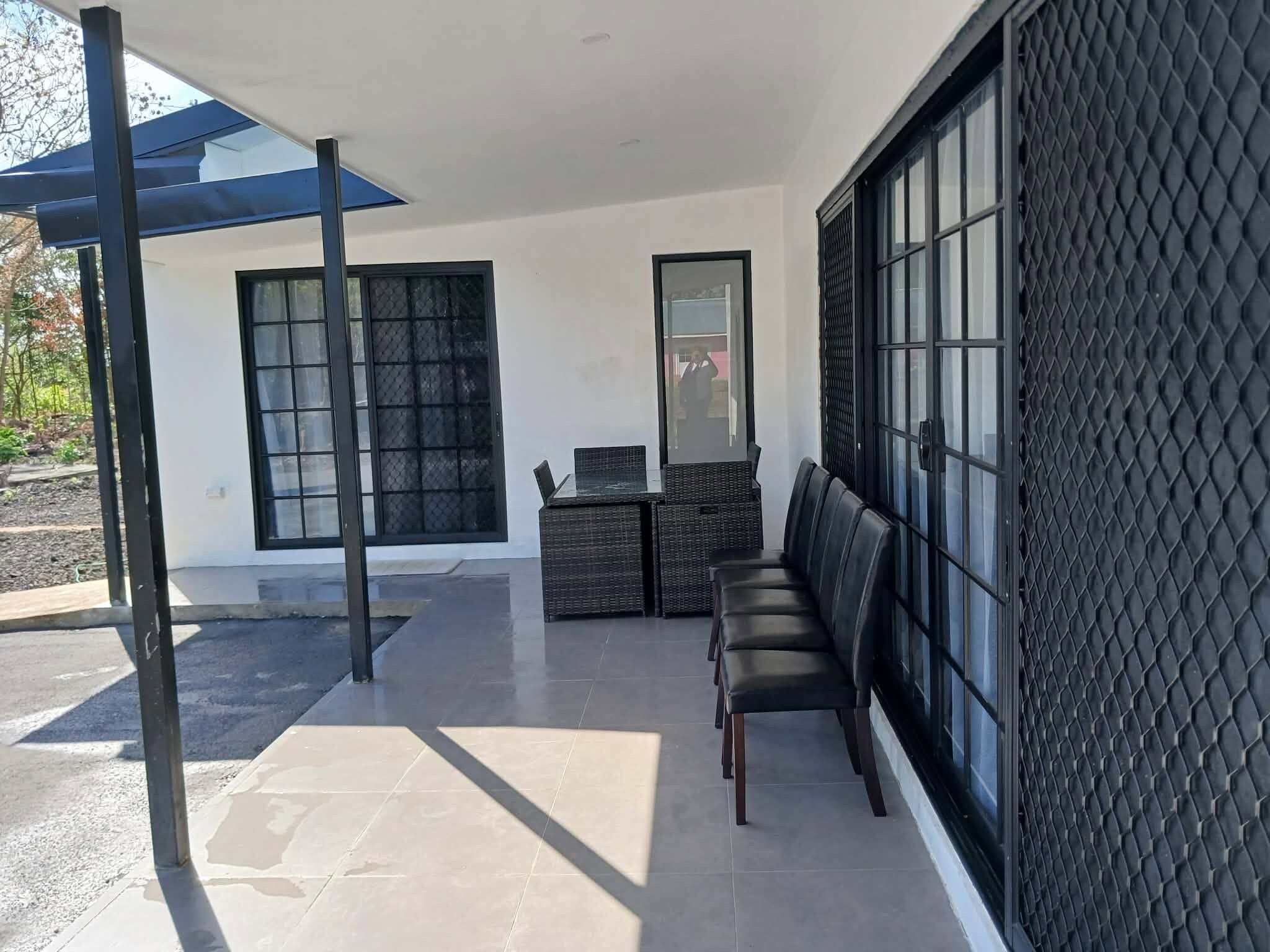 Een modern buitenzitgedeelte met een bank en een tafel, een groot raam met een zwart, gestructureerd muur, en een heldere lucht.