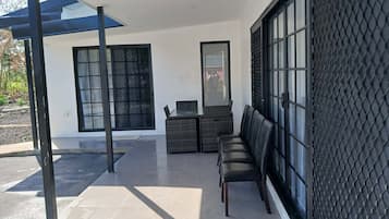 Een modern buitenzitgedeelte met een bank en een tafel, een groot raam met een zwart, gestructureerd muur, en een heldere lucht.