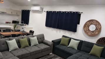 Een moderne woonkamer met grijze banken, een eettafel en een keuken met kasten en een airconditioning.
