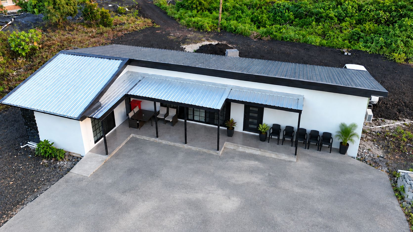 Un edificio moderno con tetto piatto, una zona relax esterna coperta con sedie e un vialetto lastricato.
