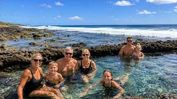 Un grupo de personas en una piscina de agua cristalina rodeada de terreno rocoso, con vista al océano.