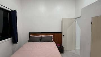 Um quarto com cama, ventilador de teto, janela com cortinas e porta.