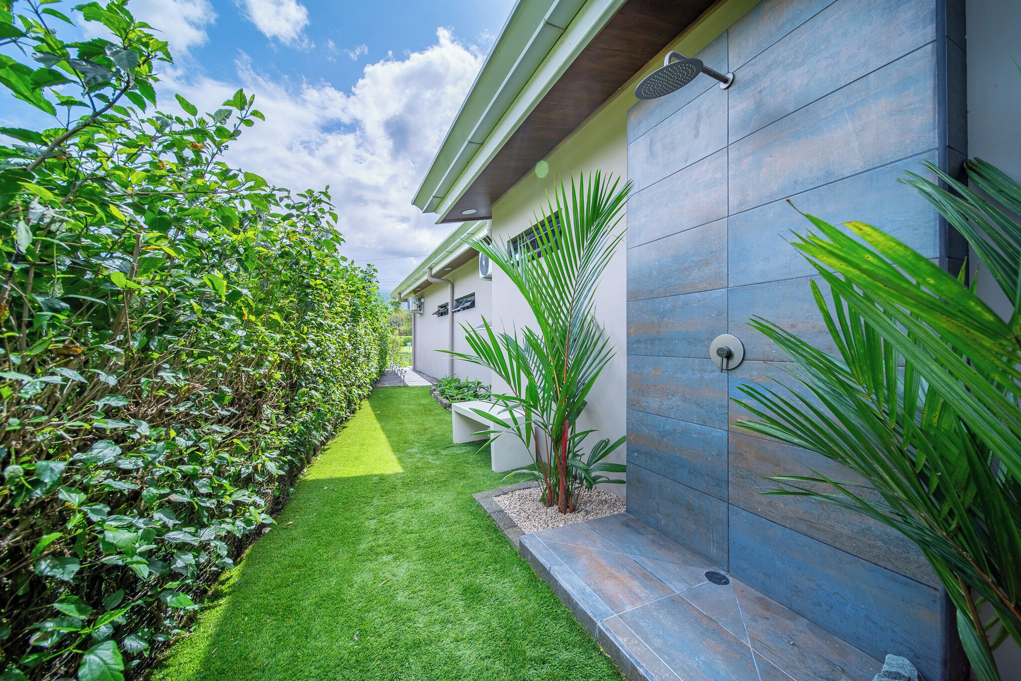 A modern building with a flat roof, a covered outdoor area with a water feature, and a well-maintained garden with a variety of plants.
