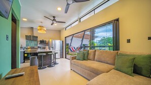 A modern living room with a sofa, a wooden table, and a kitchen in the background. - Casa Nantú - Arenal Volcano Views • Zero-Entry Pool • Sauna • 4BR/4.5BA (La Fortuna)