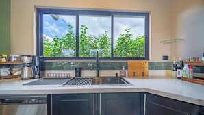 A modern kitchen with a large window, a built-in sink, and various appliances. - Casa Nantú - Arenal Volcano Views • Zero-Entry Pool • Sauna • 4BR/4.5BA (La Fortuna)