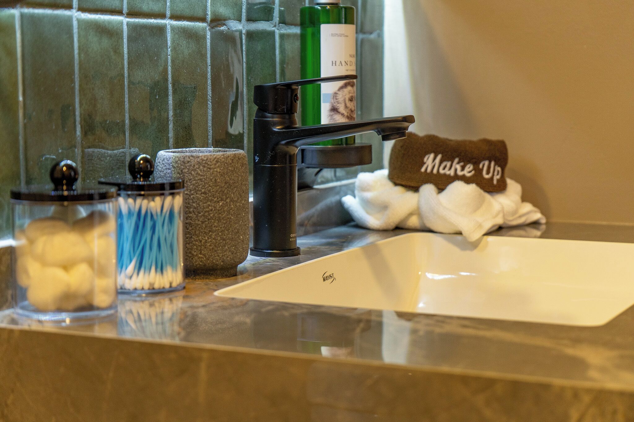 A bathroom sink with a towel rack, a soap dispenser, and a glass jar with cotton swabs.