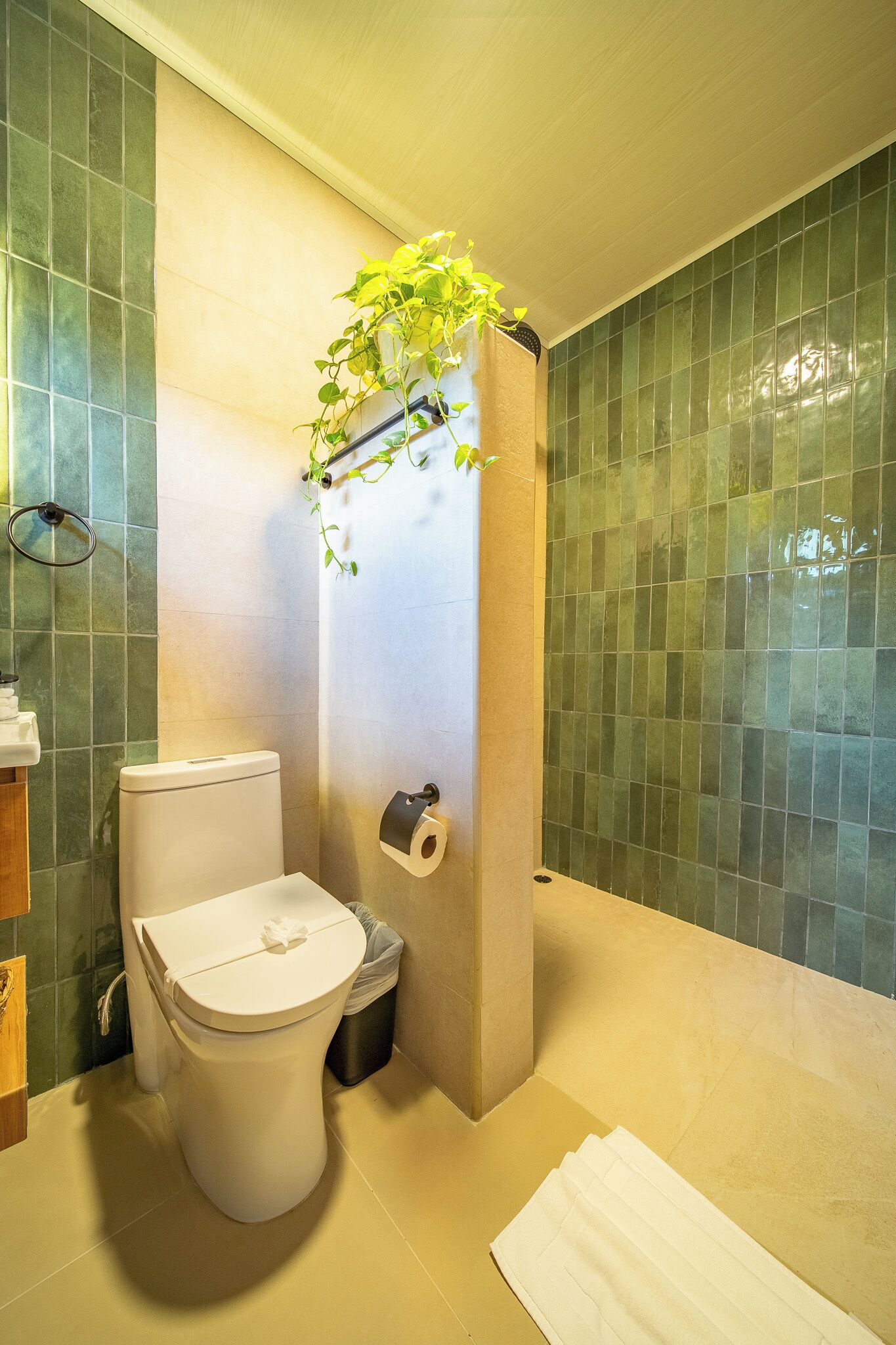 A bathroom with a toilet, a towel, a trash bin, and a toilet paper holder.