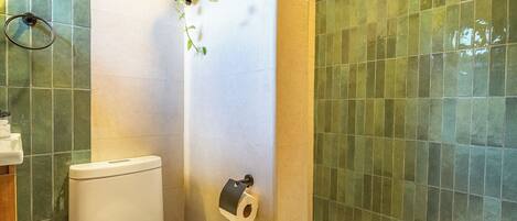 A bathroom with a toilet, a towel, a trash bin, and a toilet paper holder.