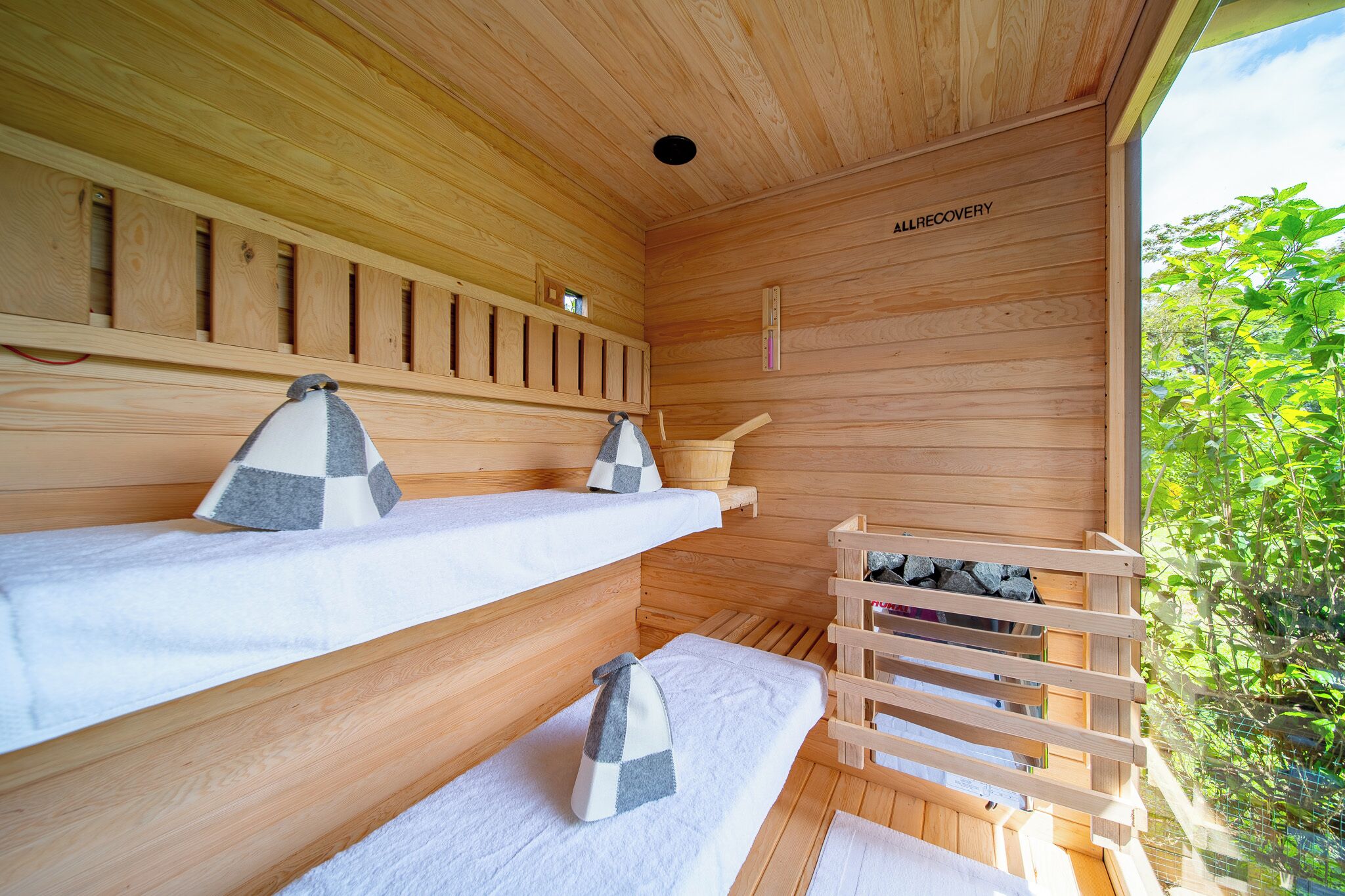 Un sauna en bois avec trois bancs, un banc en bois et un mur de sauna muni d’un thermomètre.
