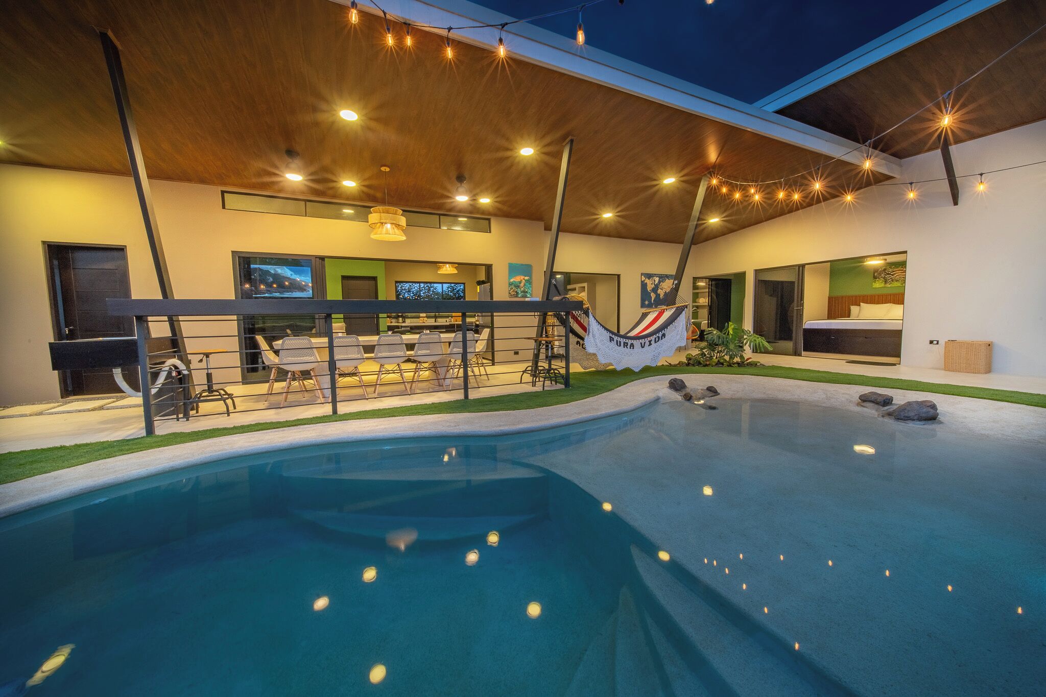 A modern indoor pool area with a hammock, seating, and a bar.