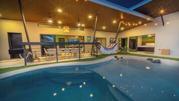 A modern indoor pool area with a hammock, seating, and a bar.
