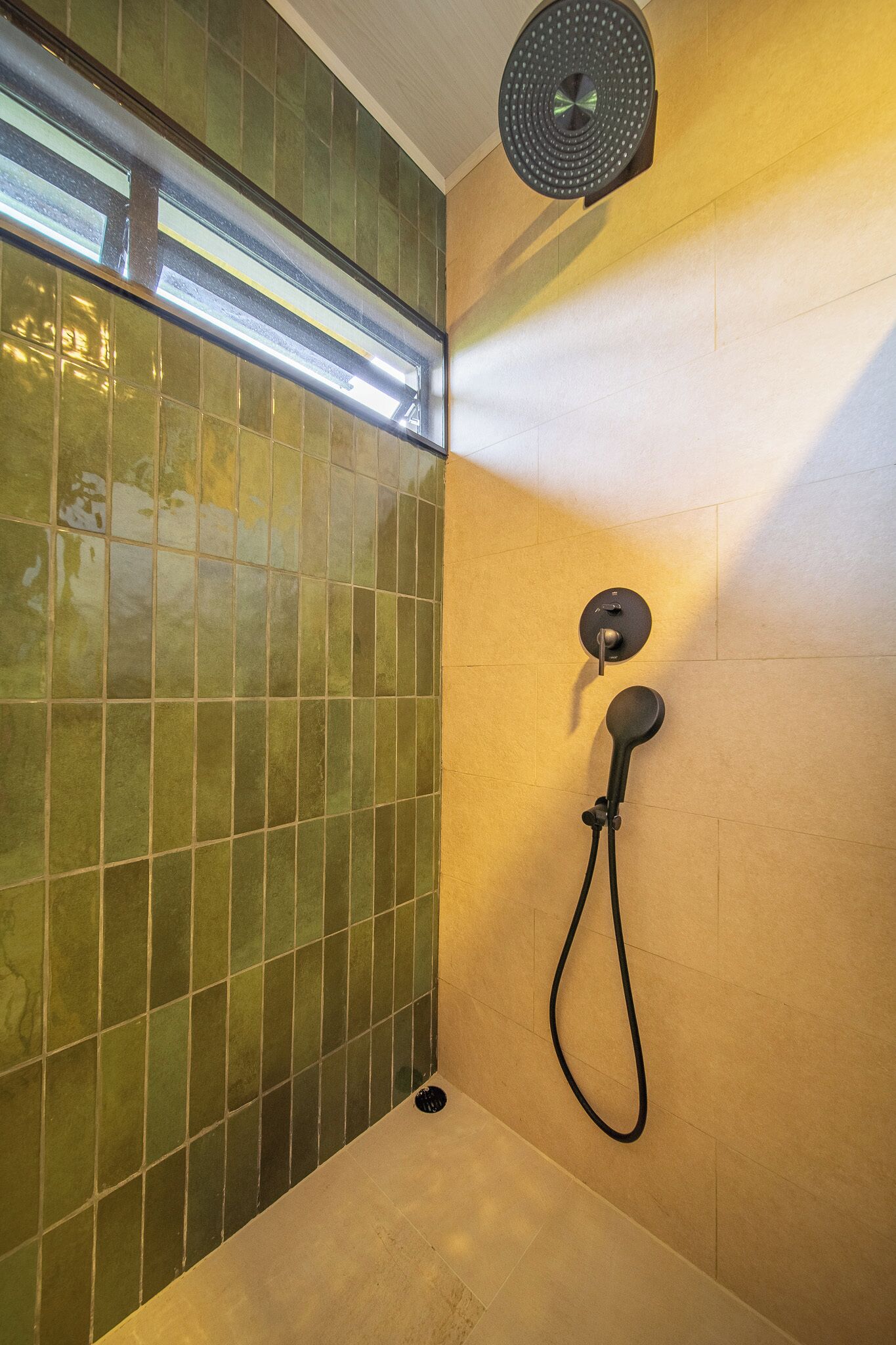 A shower area with a glass door, a wall-mounted control panel, and a ceiling light fixture.