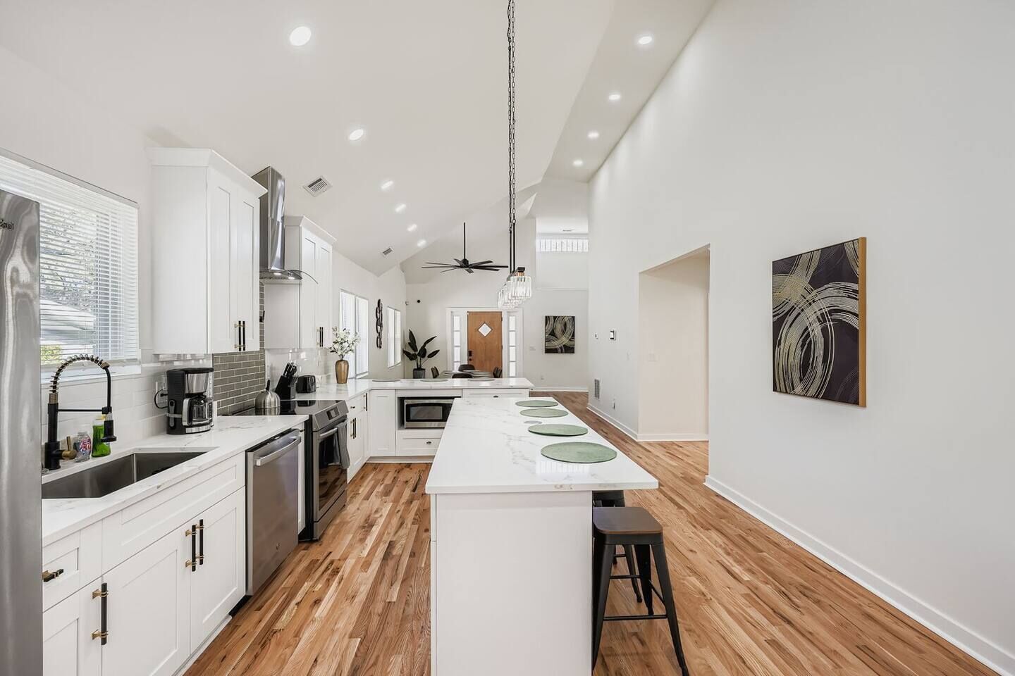 A modern kitchen with white cabinetry, a central island with green plates, and a wooden floor.