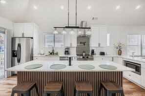 A modern kitchen with a central island, stainless steel appliances, and a hanging light fixture. - 5 king beds, 2 kitchens, 2 living rooms | East Atlanta Village (Atlanta)