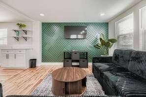 A modern living room with a green accent wall, a black sofa, a wooden coffee table, and a TV mounted on the wall. - 5 king beds, 2 kitchens, 2 living rooms | East Atlanta Village (Atlanta)