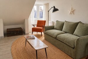 Un salon avec un canapé, un fauteuil et une lampe. Il y a une décoration en forme d’étoile sur le mur et une fenêtre avec des rideaux.