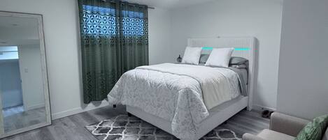 A bedroom with a bed, a sofa, a patterned rug, and a door leading to another room.