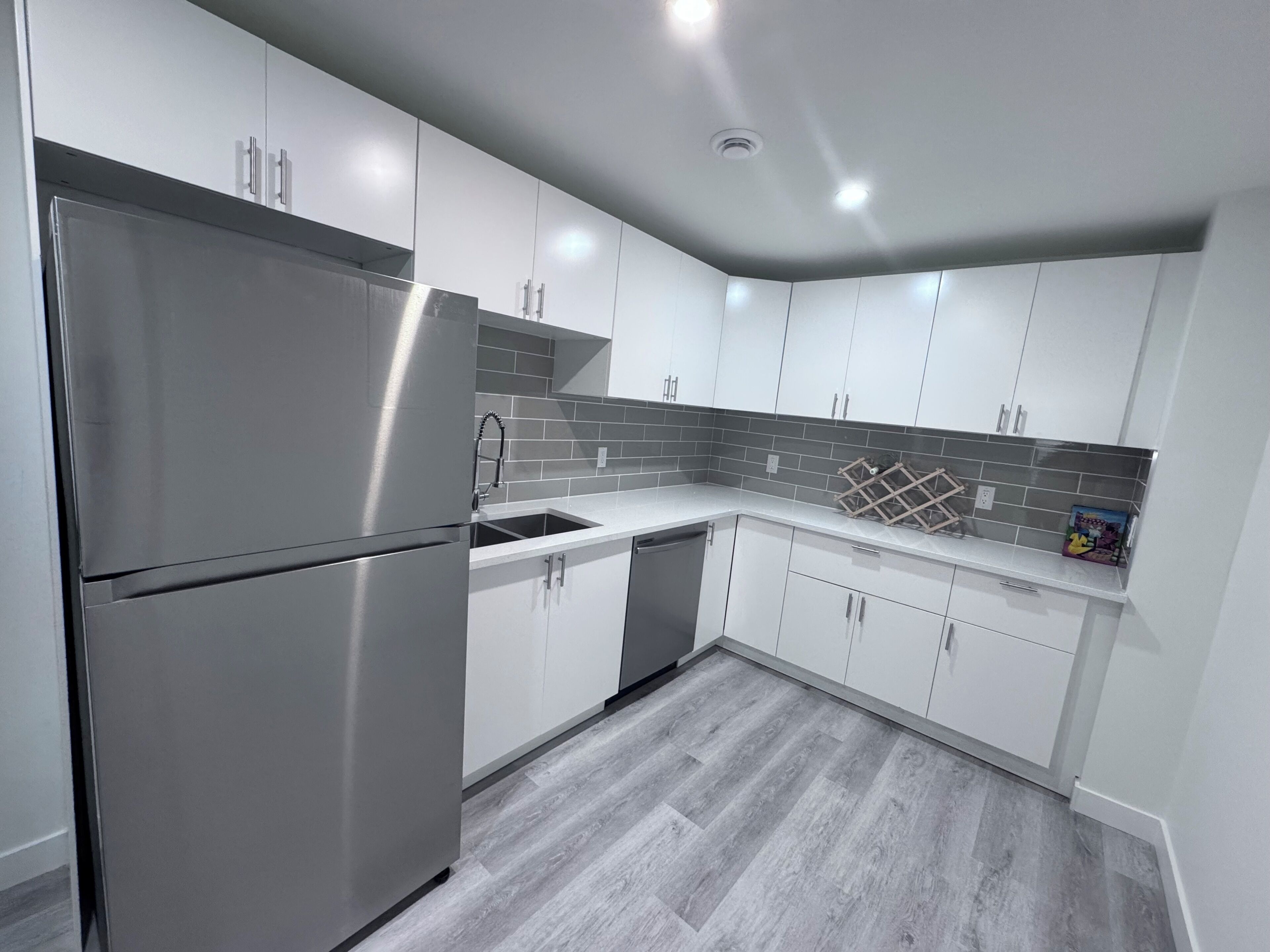 A modern kitchen with white cabinets, stainless steel appliances, and a grey tiled backsplash.
