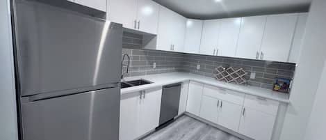 A modern kitchen with white cabinets, stainless steel appliances, and a grey tiled backsplash.