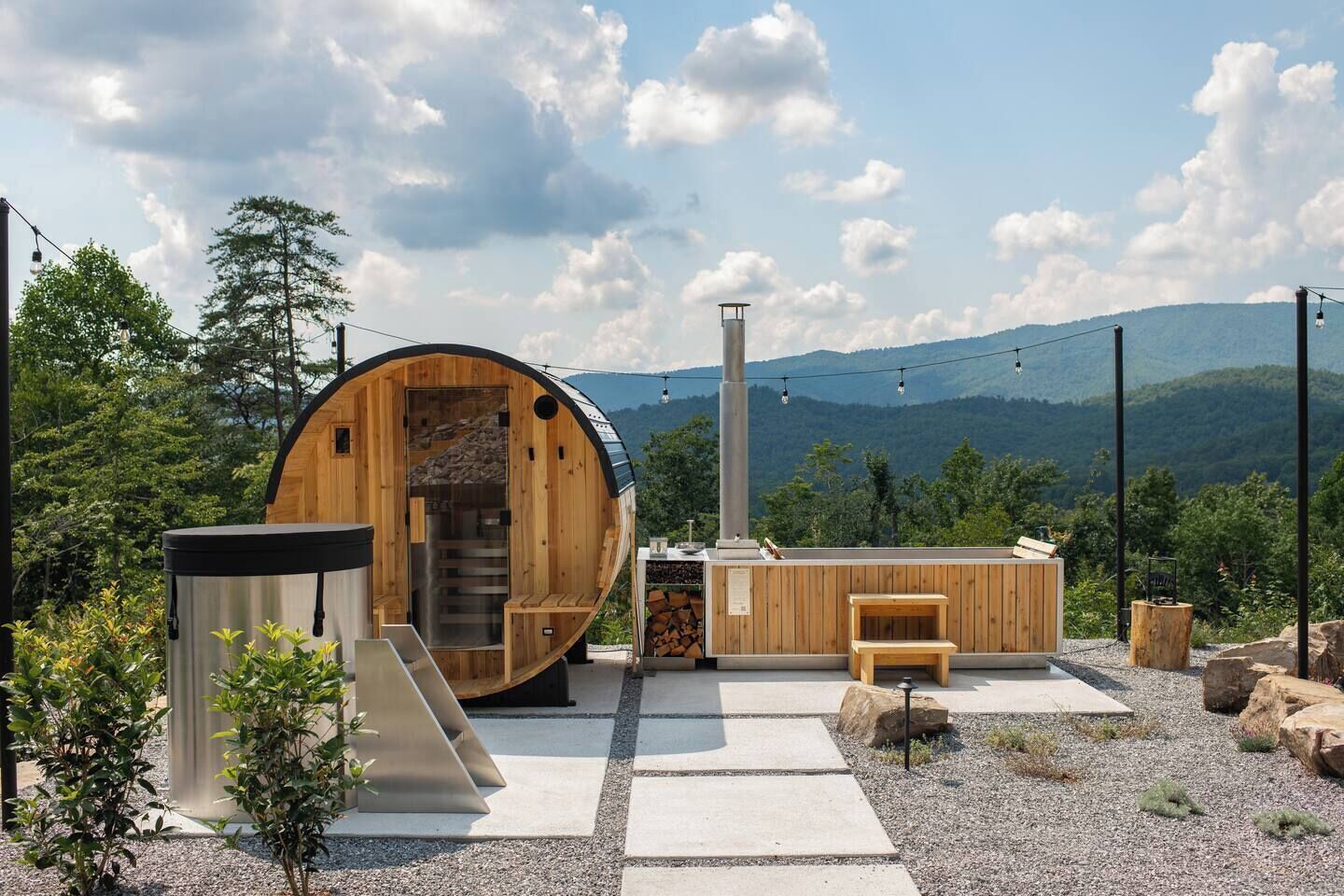 Una sauna in legno con una scala in pietra, una panchina e un piccolo tavolo, con montagne sullo sfondo.