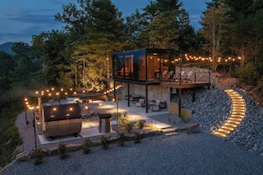 Un espacio exterior moderno con terraza, zona de estar y una pequeña construcción con paredes de vidrio.