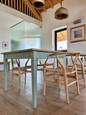 Ein Zimmer mit einem Holztisch, Stühlen, einem großen Fenster und einem Gemälde an der Wand.
