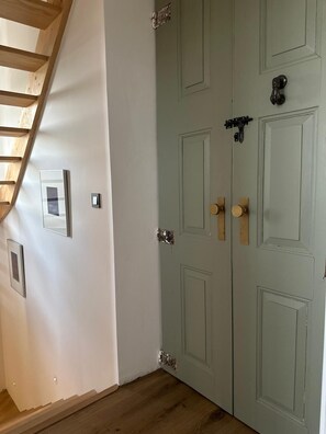 Eine Treppe mit Holzbodenstufen führt zu einer Zwischenebene, eine hellgrüne Tür mit Messingklinke und zwei gerahmte Bilder an der Wand.