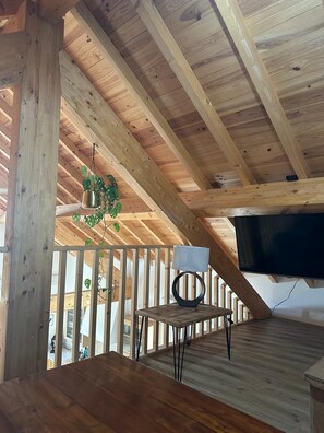 Eine Holzdachterrasse mit Fernseher, einem Tisch mit Lampe und einer hängenden Pflanze.