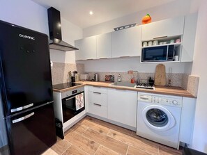 A compact kitchen with a black refrigerator, a microwave, a washing machine, and a sink. - Two-bedroom apartment with a pool and garden—between Aix-en-Provence and the Luberon—perfect for families! (Pertuis)