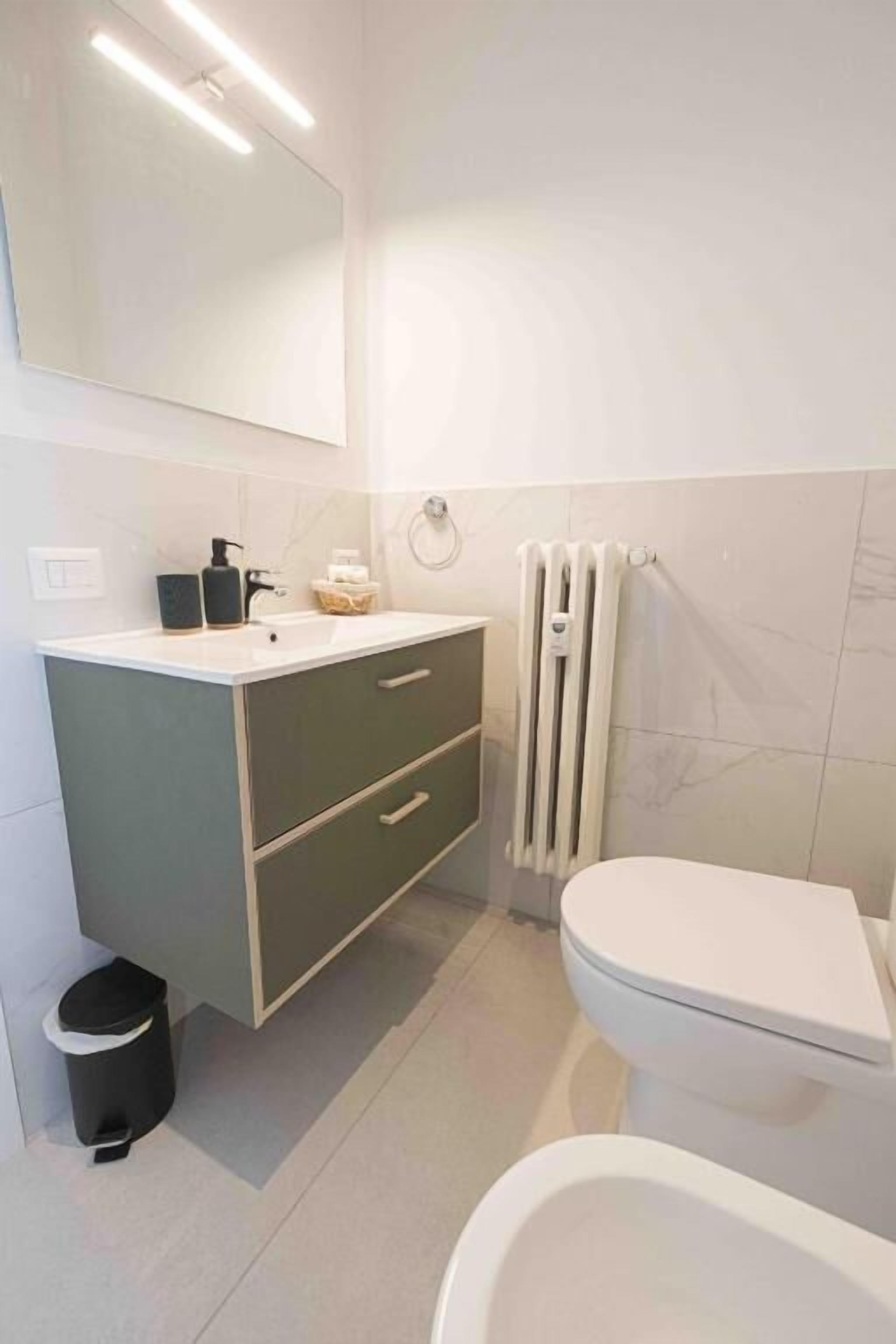 A modern bathroom with a white toilet, a vanity with a mirror, and a radiator.