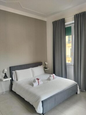 A hotel room with a bed, a nightstand, a lamp, and a window with curtains. - Metanoia Stays Prati (Rome)