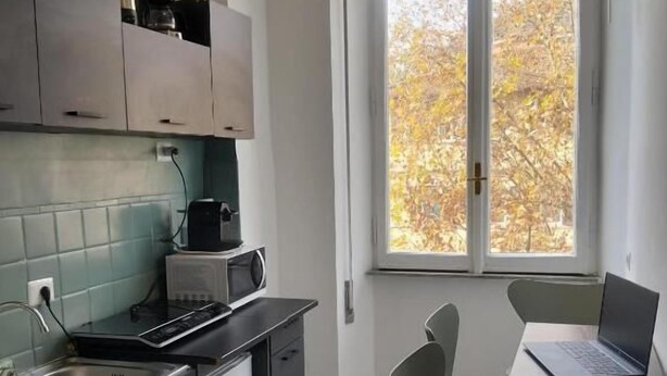 Eine kleine Küche mit Essbereich, ein Fenster mit Blick auf Bäume und ein Laptop auf dem Tisch.