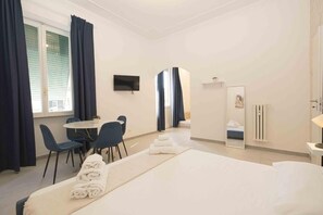 A hotel room with a bed, a desk, two chairs, a television, and a mirror. - Metanoia Stays Prati (Rome)