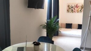 Ein modernes Zimmer mit rundem Tisch, einem Laptop, einer Topfpflanze und einem an der Wand montierten Flachbildfernseher.