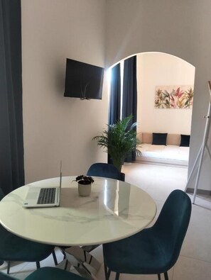 A modern room with a round table, a laptop, a potted plant, and a flat-screen TV mounted on the wall. - Metanoia Stays Prati (Rome)