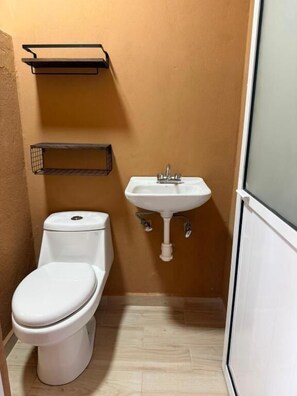 A small bathroom with a toilet, sink, and two wall-mounted shelves.