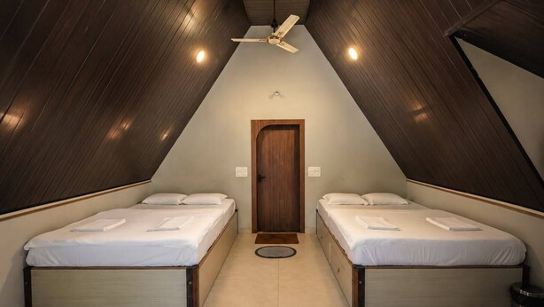 A triangular room with two beds, a ceiling fan, and a door.