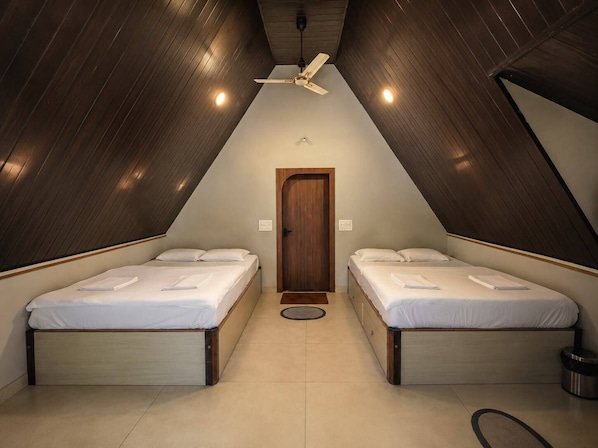 A triangular room with two beds, a ceiling fan, and a door. - Hills and Chills Nature Stay (Sakleshpur)
