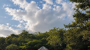 A pavilion with a tiled roof, surrounded by a grassy area and trees.