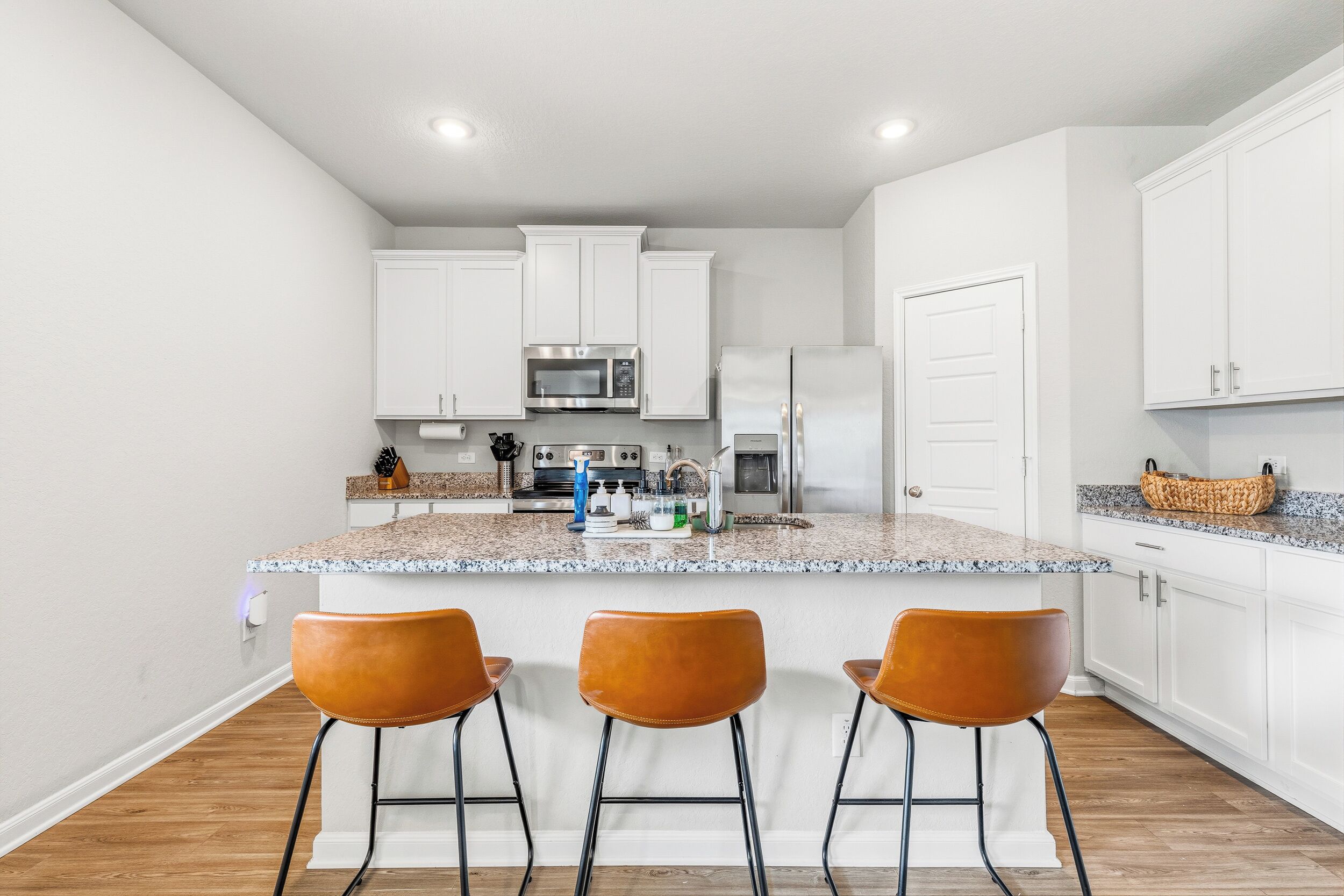 A modern kitchen with white cabinets, a granite countertop, and three brown bar stools.