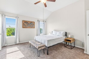 Ein Schlafzimmer mit einem Bett, einem Nachttisch, einer Bank, einem Deckenventilator und einem Fenster mit Vorhängen.