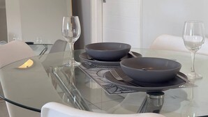 Moderni ruokailutila, jossa on lasipöytä, valkoiset tuolit ja tummat kulhot.
