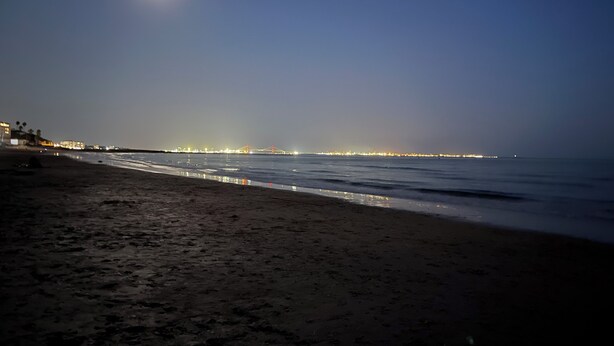 Uma praia à noite, com uma ponte ao longe e luzes da cidade ao longo da orla.