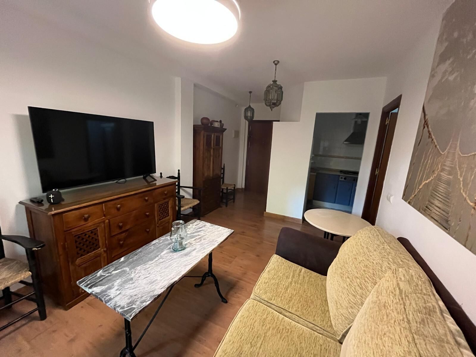 Un salon comprenant un téléviseur, un meuble en bois, une table basse en marbre et un canapé.
