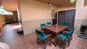 Um alpendre coberto com uma mesa e cadeiras de madeira, um lustre pendurado e piso de azulejos.