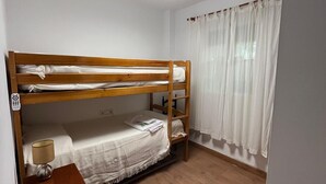 Quarto com beliche, cabeceira de madeira, mesa de cabeceira com luminária, janela com cortinas leves e luminária no teto.