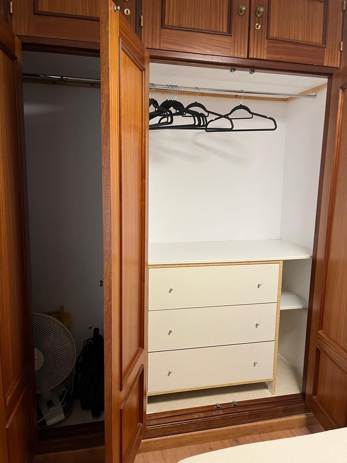 A wooden wardrobe with a hanging rod and three drawers.